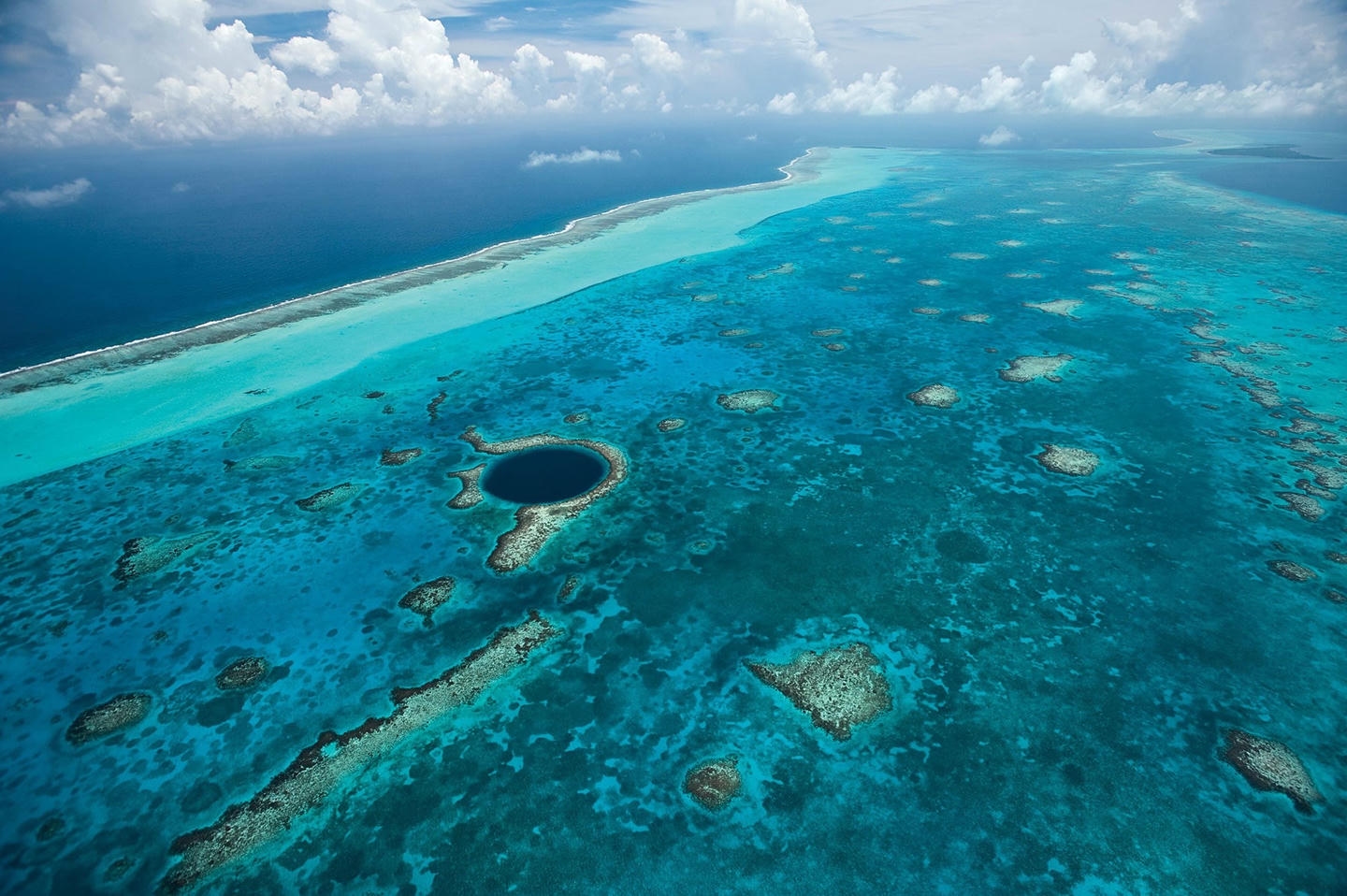 Wide aerial view of the Great Blue Hole from the north looking southward, with the Belize Barrier Reef dividing the waters on the left side of the image. Wide aerial view of the Great Blue Hole from the north looking southward, with the Belize Barrier Reef dividing the waters on the left side of the image.