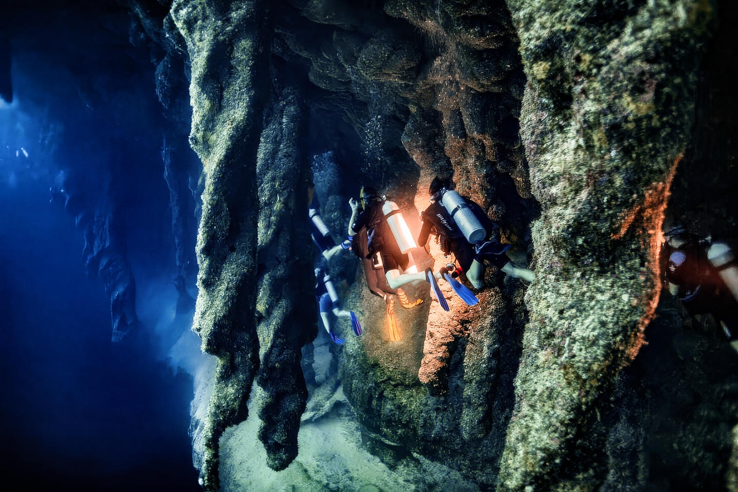 Four divers diving through a series of stalactites deeper within the Great Blue Hole. Four divers diving through a series of stalactites deeper within the Great Blue Hole.